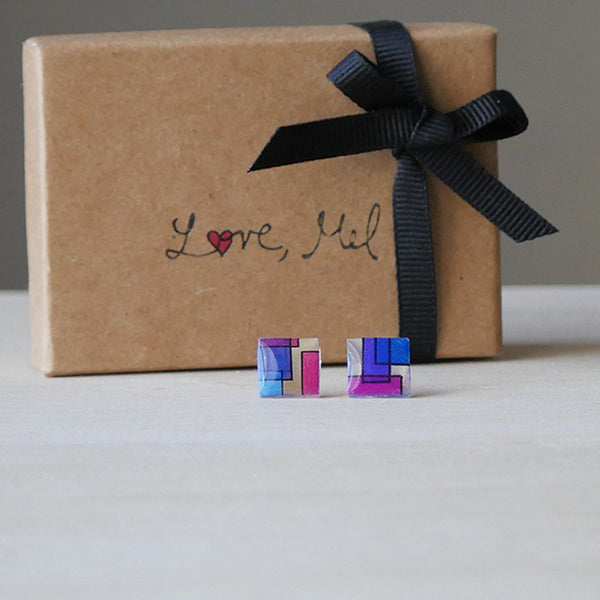 Square stud earrings with blue, fuchsia, and purple layered squares on a translucent backdrop